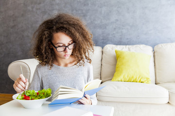 Curly hair teenage girl reading book and eating salad