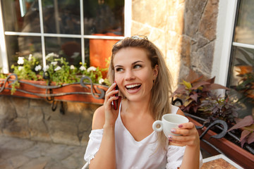 Fototapeta na wymiar Happy woman with cup of coffee and red smart phone smiling in cafe. Young worker, freelancer or bloger with smile. Business woman calling on phone after work
