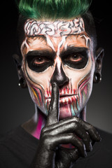 Man with frightened halloween makeup and black palm. Close up view of male with colored skeleton makeup.