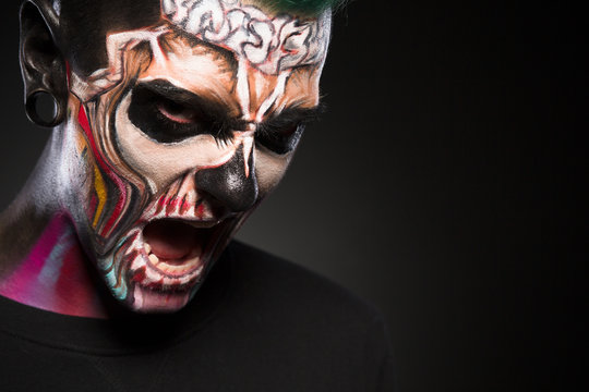 Face art, proffesional colored makeup for Halloween. Monster makeup, man with zombie face, studio portrait.