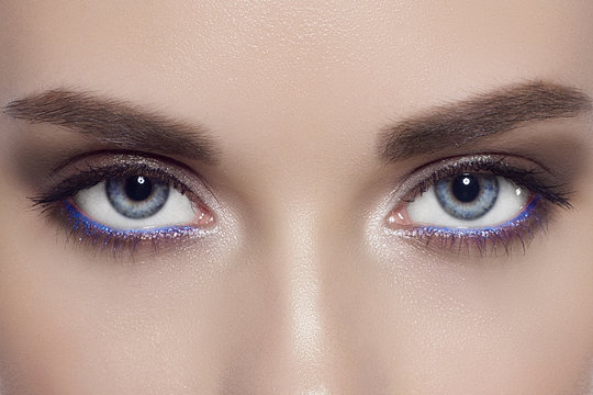 The macro photo of blue female eyes with a fashionable make-up, long eyelashes and equal dense eyebrows. Correction of eyebrows, sight, cosmetology, lenses, extension of eyelashes, permanent make-up