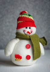 Smiling snowman toy dressed in scarf and cap on abstract bokeh background.