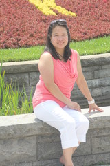  Mature, Asian woman sitting on a low stone wall posing for photos.      