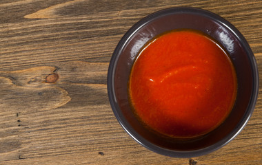 Red hot chilli sauce in white ceramic bowl on a wooden background. with copy space. top view