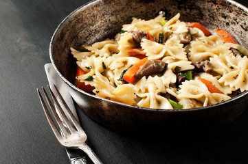 fresh cooked pasta with mushrooms and vegetables in a pan with a vintage fork and knife near by