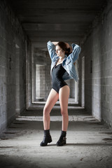 Concept: gritty, millennial. Gorgeous beautiful young girl wearing body and jeans jacket photoshoot in abandoned construction of building presenting the contrast of fashion and grunge.