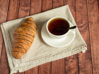 Breakfast croissant and tea on a textile napkin. Dark wooden background.