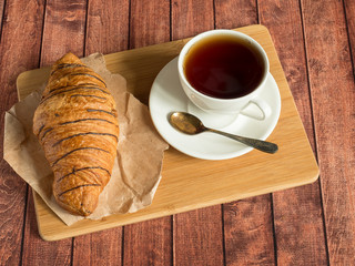 Breakfast croissant and tea on a textile napkin. Dark wooden background.
