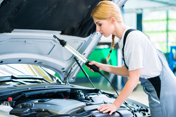 Female mechanic examine car engine with light in workshop 