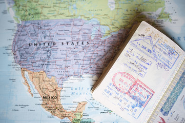 (Selective focus) Close-up view of a passport with entry stamps on a blurred geographical map of the world. The map shows the United States an Mexico