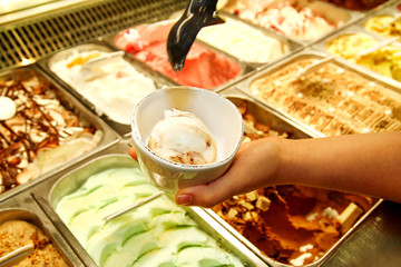 Female hand with scoop takes ice cream from the fridge and serving in ceramic white cups. Woman taking scoop of tasty ice cream. Fridge with ice cream. Woman works in ice cream shop. Pastry shop.