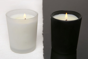 Obraz na płótnie Canvas White and black candles. Two burning candles on black table with white napkin.