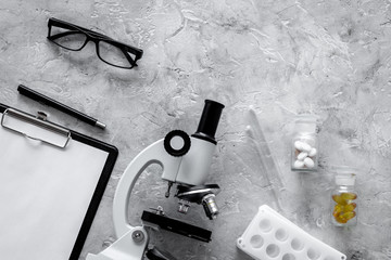 Doctor's workplace. Microscope, tablet, pills on grey stone background top view copyspace