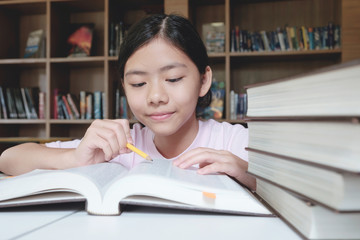 Girl reading and writing in library of school.