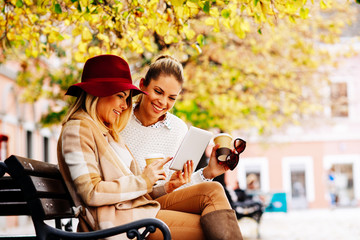Two women using digital tablet on the bench in the city center