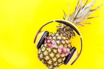 Pineapple-hipster in pink glasses and headpones on yellow background top view copyspace