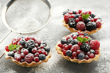 Tasty tartlets with berries and powdered sugar on grey wooden table