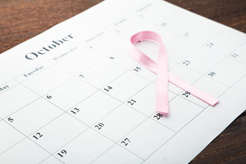 Pink ribbon with calendar sheet on wooden table