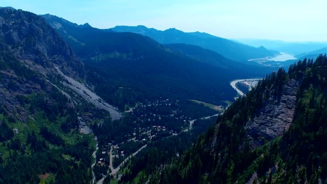 Sideways moving shot of a city in rocky, green alpine mountains in summertime, revealing vast vistas of beautiful nature, establishing shot