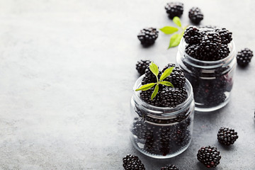Fototapeta na wymiar Sweet blackberries in bottles on grey wooden table