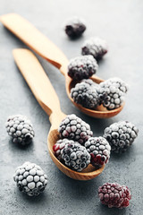 Frozen blackberries in spoons on grey wooden table