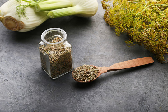 Fennel seeds in glass jar and spoon on grey background