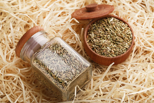 Fennel seeds in glass jar and wooden bowl on raffia background