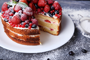 Homemade biscuit cake with berries and powdered sugar on grey wooden table