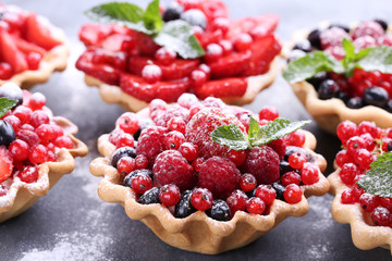 Dessert tartlets with berries and powdered sugar on grey wooden table