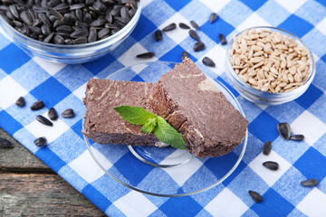 Tasty pieces of halva with bowl of seeds on blue napkin