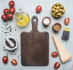 Preparation of salad with tomatoes, olives, butter and various seasonings, ingredients are lined around the cutting board on a blue wooden background