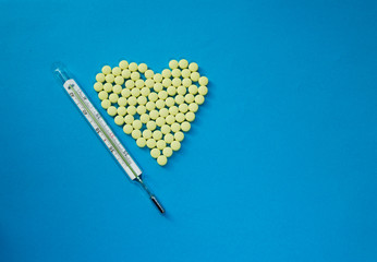 Yellow pills in shape of heart and Medical thermometer