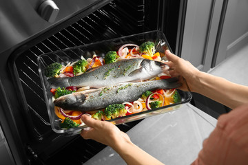 Femme mettant une plaque de cuisson avec du poisson et des légumes au four