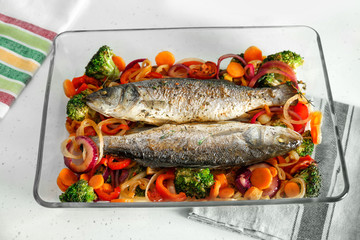 Baking tray with tasty fish and vegetables on kitchen table