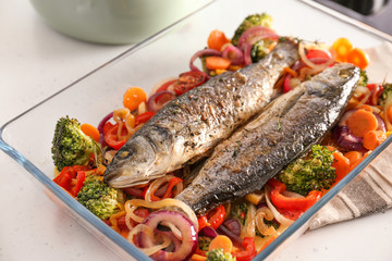 Baking tray with tasty fish and vegetables on kitchen table
