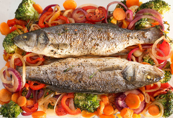 Tasty baked fish with vegetable garnish, top view
