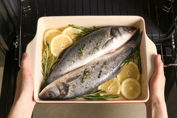 Woman putting baking tray with fish into oven