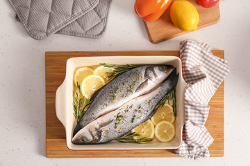 Baking tray with uncooked fish, lemon slices and herbs on kitchen table