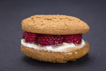 Oat cookies with raw raspberry, honey and soft cheese on the background of black slate , close up