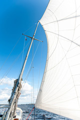 Fototapeta premium White yacht sails in sunlight on blue cloudy sky background.
