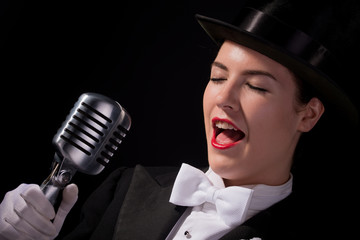 Beautiful young woman dressed in vintage top hat and tails with old microphone.