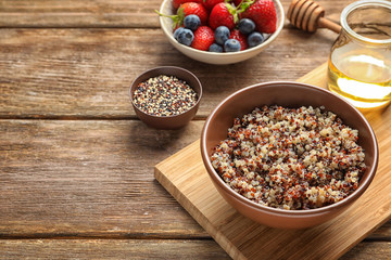 Bowl with tasty quinoa on wooden board