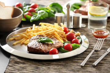 Silver plate with delicious steak and fries on table in restaurant