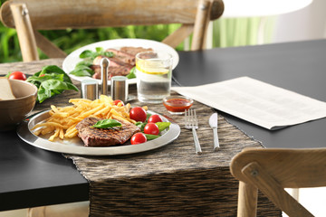 Silver plate with delicious steak and fries on table in restaurant