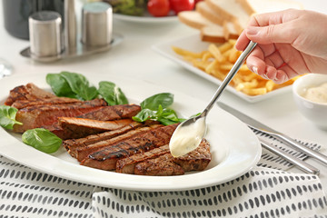 Woman adding sauce to delicious grilled steak in restaurant