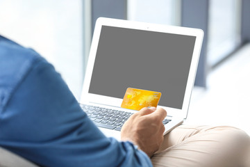 Man holding credit card while using laptop indoors