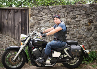 Fototapeta na wymiar The biker sits on a motorcycle in the yard of his house