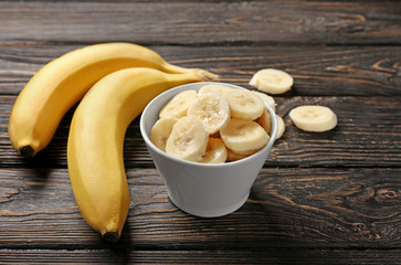 Yummy bananas and bowl with slices on wooden background
