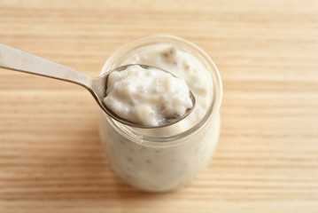 Spoon and jar with delicious chia seed pudding on table