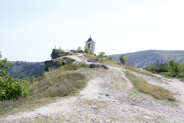 A temple on the slope near green tree and golden grass in sunny day. Orthodox church with cross on...